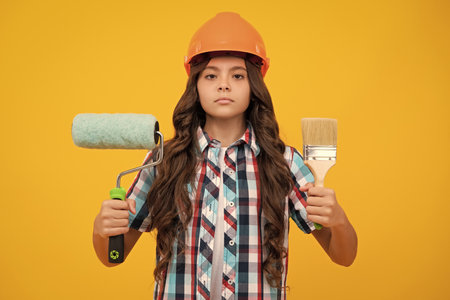 Kids renovation and building concept. Little girl in protective helmet and paint brush for painting walls.の写真素材