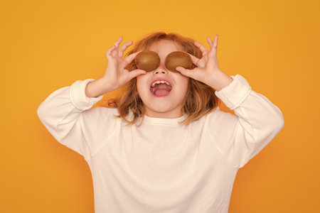 Child hold kiwi in studio. Kiwi fruit. Studio portrait of cute kid boy with kiwi isolated on yellow.
