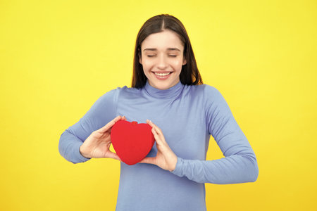 Love sign symbols for happy womens, valentines day or birthday. Beautiful amazing woman cuddle paper card heart shape, dreamy isolated on yellow background. Love concept.の写真素材