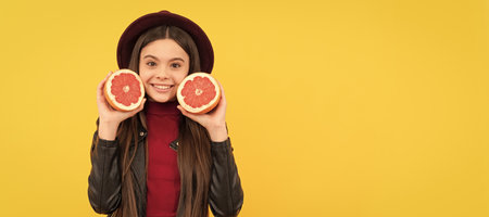 happy teen girl in hat and leather jacket hold cut grapefruit. Child girl portrait with grapefruit orange, horizontal poster. Banner header with copy space.の写真素材