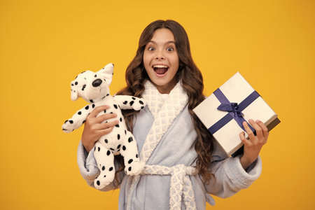 Teenager child holding gift box on yellow isolated background. Gift for kids birthday. Christmas or New Year present box. Amazed teen girl. Excited expression, cheerful and glad.の写真素材