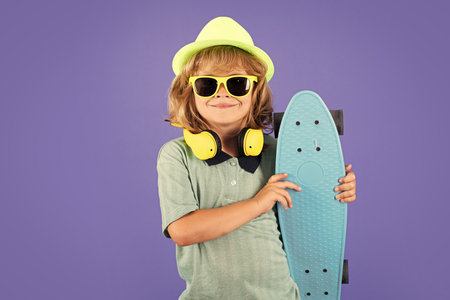 Happy child boy holding skateboard over blue background isolated. Studio portrait of fashion kids.の写真素材