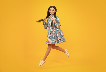Full length little overjoyed teen girl 12, 13, 14 year old jump and fly isolated on yellow background studio.の写真素材