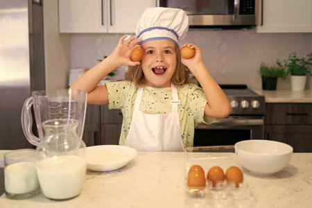 Child chef cook. Funny child stand at kitchen table have fun baking, doing bakery preparing food at home kithen. Healthy food. Little chef preparing healthy meal.の写真素材