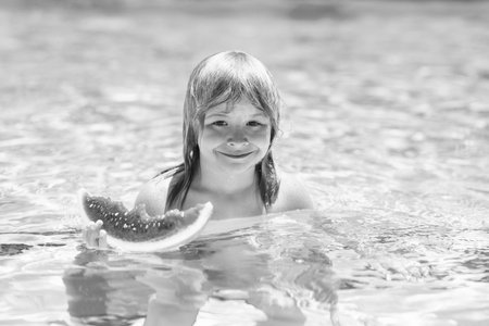 Child with watermelon in swimming pool. Kids eat summer fruit outdoors. Child playing in the swimming pool. Summer kids activity. Little child playing in blue water. Summer watermelon fruit for children.の写真素材