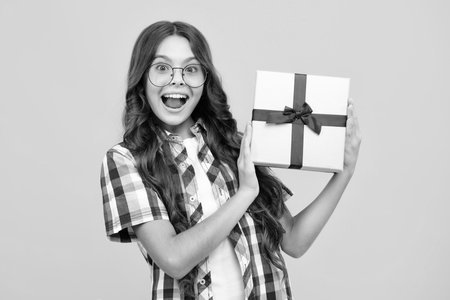 Amazed teen girl. Child with gift present box on isolated background. Presents for birthday, Valentines day, New Year or Christmas. Excited expression, cheerful and glad.の写真素材