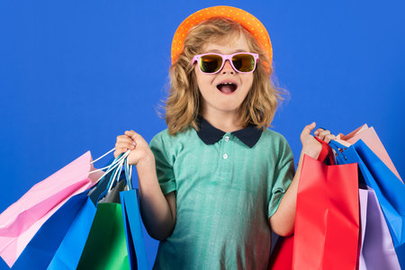 Little kid shopper. Kid boy in fashion clothes on shopping. Child with shopping packages. Shopper child with shopping bag posing shopping bags on studio background.の写真素材