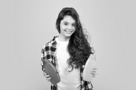 Teenager child girl with bottle shampoo conditioners or shower gel. Kids hair care. Hair cosmetic product, shampoo bottle. Happy teenager, positive and smiling emotions of teen girl.の写真素材