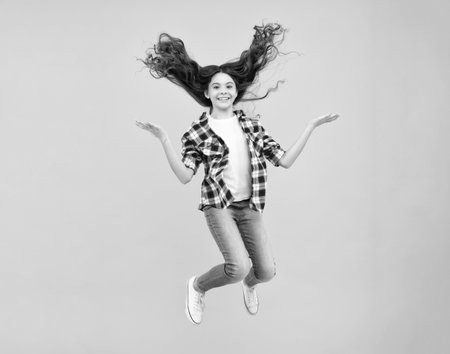 Teenager face with crazy movement hair. Happiness, freedom, motion and child. Young teenager girl jumping in air over yellow background.の写真素材