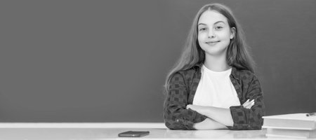 cheerful kid sitting in classroom at blackboard, september. Portrait of schoolgirl student, studio banner header. School child face, copyspace.の写真素材