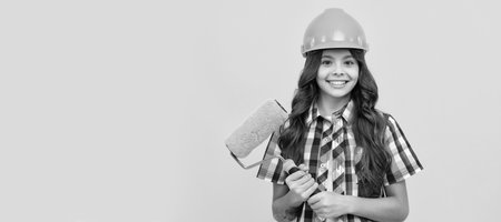 making surface repair. happy girl hold paint roller. child in helmet. roller brush for decoration. Child builder in helmet horizontal poster design. Banner header, copy space.の写真素材