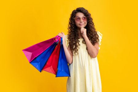 Child girl hold shopping bag enjoying sale isolated on yellow background. Portrait of teenager girl is ready to go shopping. Summer shopping sale. Thinking teenager girl, thoughtful emotion.の写真素材