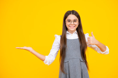 Look at advert. Teenager child points aside shows blank copy space for text promo idea presentation, poses against yellow background.の写真素材