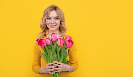 glad young girl with spring tulip flowers on yellow backgroundの写真素材