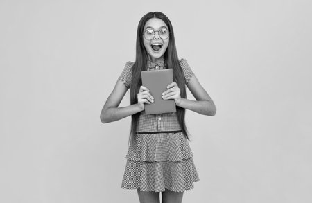 Amazed teen girl. Schoolgirl with copy book posing on isolated background. Literature lesson, grammar school. Intellectual child reader. Excited expression, cheerful and glad.の写真素材