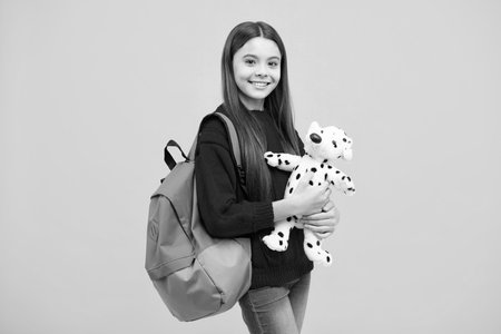 Funny school girl with toy isolated on yellow background. Happy childhood and kids education.の写真素材