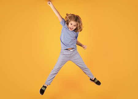 Full body of little child jump wear casual t-shirt and jeans isolated on yellow background.の写真素材