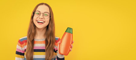 presenting cosmetic product for teen. kid in glasses use shower gel. Banner of child girl hair care, studio poster header with copy space.の写真素材
