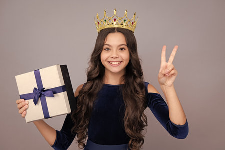 Teenager kid with present box. Teen girl princess in crown giving birthday gift. Present, greeting and gifting concept. Happy face, positive and smiling emotions of teenager child.の写真素材
