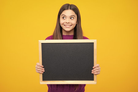 School sales board. Cheerful teenage girl kid hold blackboard chalkboard with copy space.の写真素材