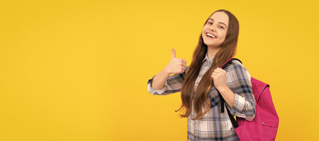 happy teen girl in checkered shirt carry backpack showing thumb up on yellow background. Portrait of...