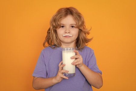 Healthy drink with calcium and protein for kids. Small boy drink a glass of milk with funny emotions on yellow background. Child drinking milk, studio portrait. Cute kid hold a glass of milk.の写真素材