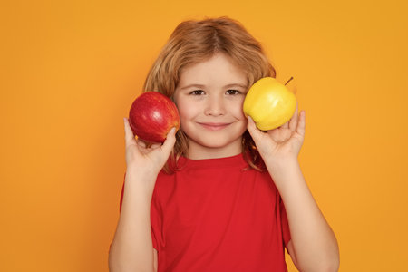 Vitamin and healthy fruits for kids. Kid in red t-shirt with apple in studio. Studio portrait of cute child hold apple isolated on yellow background.の写真素材