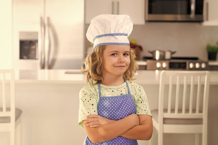 Portrait of funny child chef in kitchen. Children cooking in the kitchen. Funny kid chef cook cookery at kitchen. Chef kid boy making healthy food. Portrait of little child in chef hat.の写真素材
