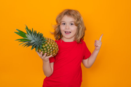 Kid with pineapple in studio. Studio portrait of cute child hold pineapple isolated on yellow background.の写真素材