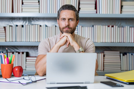 Teachers day. Teacher tutor using laptop in school classroom. Knowledge, education. Man with book...