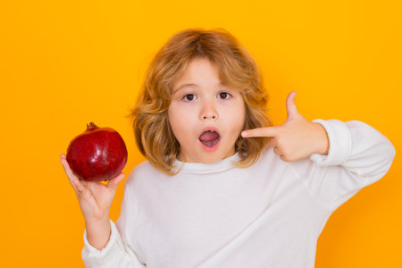 Kid hold red pomegranate in studio. Pomegranate fruit. Studio portrait of cute child with pomegranate isolated on yellow background.の写真素材
