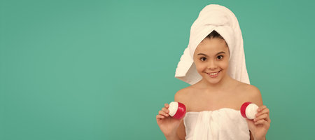 Girl with healthy skin, facial treatment, happy teen girl in bath tower presenting body cosmetic. Cosmetics and skin care for teenager child, poster design. Beauty kid girl banner with copy space.の写真素材
