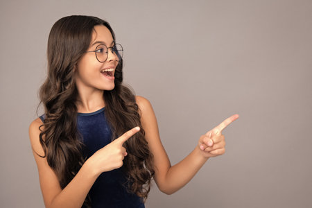 Wow, its unbelievable. Shocked teenager child pointing aside at copy space. Teen girl pointing with...