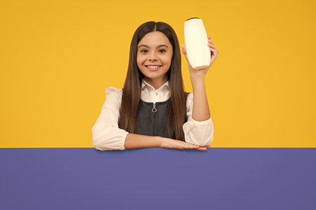 Teenager child girl with bottle shampoo conditioners or shower gel. Kids hair care. Hair cosmetic product, shampoo bottle. Happy girl face, positive and smiling emotions.の写真素材