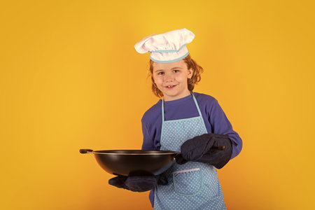 Child chef cook with cooking pan. Child chef cook prepares food on isolated studio background. Kids cooking. Teen boy with apron and chef hat preparing a healthy meal.の写真素材