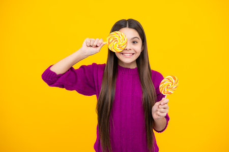 Teen girl hold lollipop caramel on yellow background, candy shop. Teenager with sweets suckers.の写真素材