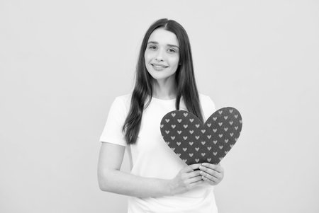 Portrait of pretty smiling woman holding paper heart in her hands on yellow background. Love concept.の写真素材