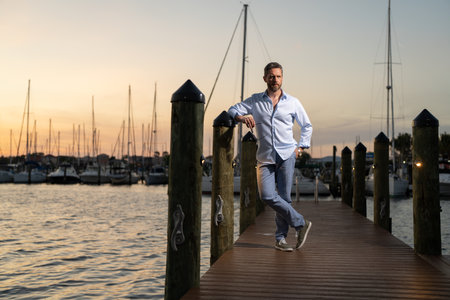 Millennial 40s man near the yacht. Portrait of fashion model outdoor. Fashion male posing near yachts. Fashion man in urban style. Handsome hispanic man at yacht club. Man in gulf near luxury yacht.の写真素材