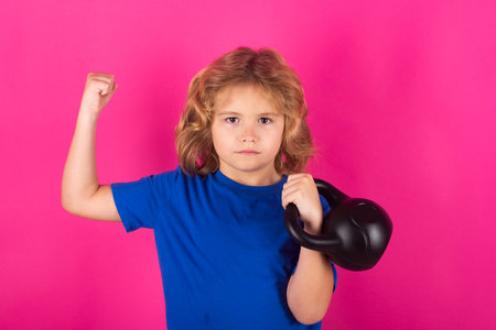 Kid with kettlebell in studio on red pink background. Sport activities at leisure with children. Blonde boy holding dumbbells. Sports exercises for children. Funny child lifting the kettlebell.の写真素材