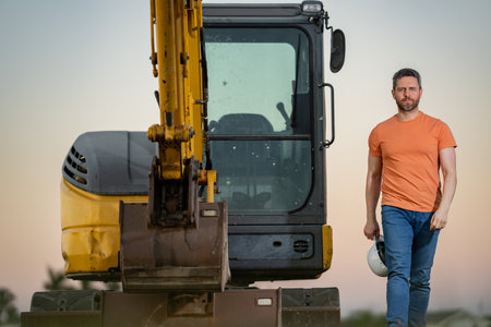 Builder with excavator for construction at the construction site. Machinery tractor with builder at buildings background. Excavator builder worker. Builder with helmet on construction site.の写真素材
