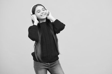 Child listening music with headphones. Girl listening songs via wireless earphones. Headset device accessory. Stylish teenage girl listening to music.の写真素材
