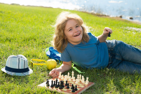 Kid playing chess game in backyard, laying on grass. Concentrated child play chess. Kid playing board game outdoor. Logic game for kids and logical thinking.の写真素材