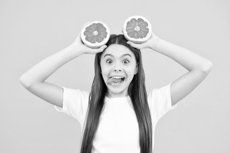 Funny face. Teenage girl holding a grapefruit on a yellow background.の写真素材