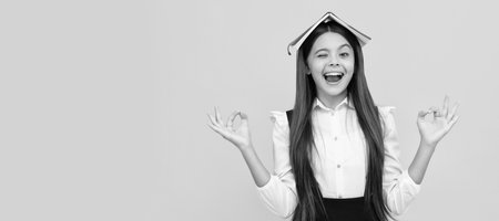 Absorbing the knowledge. Happy school girl hold book on head making mudra gesture. Knowledge day. Portrait of schoolgirl student, studio banner header. School child face, copyspace.の写真素材