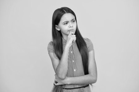 Thinking pensive clever teenager girl. Thoughtful teenager child thinking, pensive child making idea, posing isolated on yellow isolated background. Kid curious creative think about creating plan.の写真素材