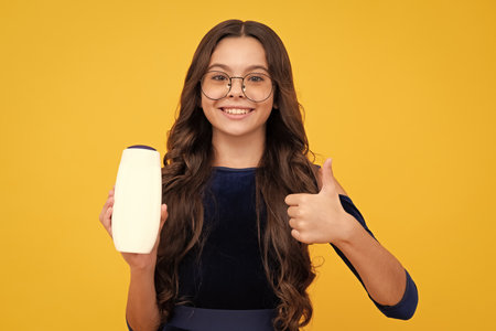 Teenager child girl showing bottle shampoo conditioners or shower gel isolated on yellow background. Hair cosmetic product. Mock up bottle. Happy face, positive and smiling emotions of teenager girl.の写真素材