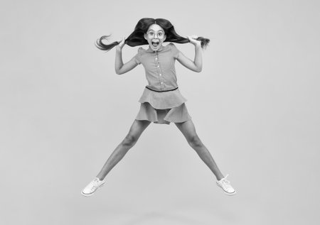 Amazed teenager. Full length overjoyed teenager kid girl 12 13 14 year in casual wear jumping old isolated on yellow background studio. Funny jump. Child in summer movement dress.の写真素材