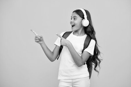 Amazed teen girl. School girl in headphones on isolated studio background. School and music concept. Excited expression, cheerful and glad.の写真素材