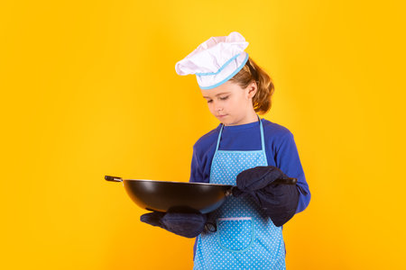 Child chef cook with cooking pan. Child wearing cooker uniform and chef hat preparing food on kitchen, studio portrait. Cooking, culinary and kids food concept.の写真素材