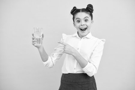 Teenager girl drinking water from glass on blue background. Daily life health. Drink water for health care and body balance. Thirsty kid, dehydration. Amazed teenager. Excited teen girl.の写真素材